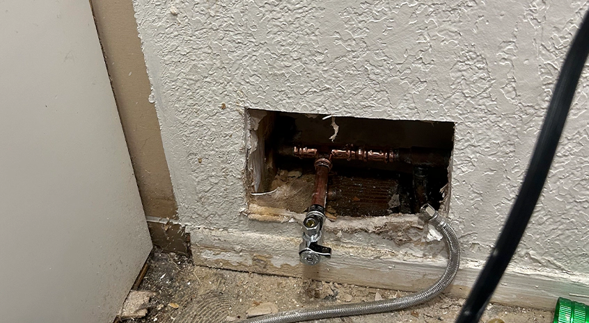Exposed copper water pipe with a small active leak dripping into a bucket