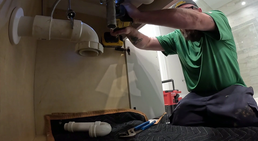 Plumber working under a sink with tools and pipes visible.