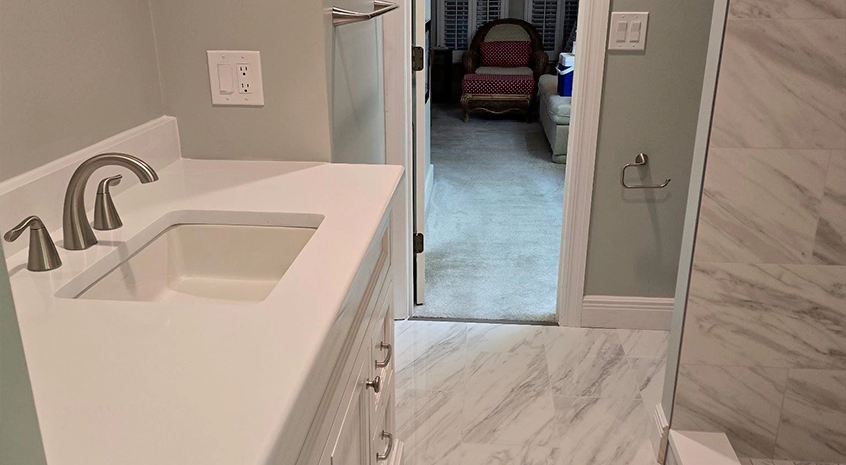White bathroom interior with marble floor and countertop, silver faucet, and adjacent room.