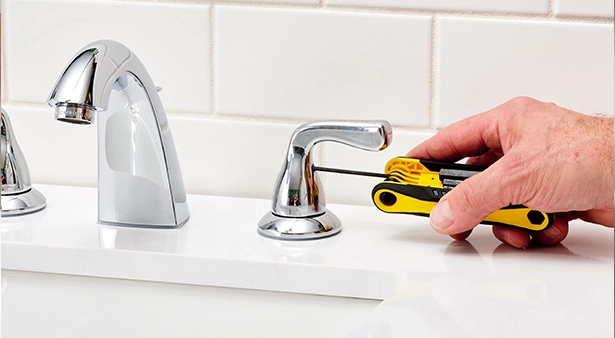 Chrome faucet installation using a yellow multi-bit screwdriver in a bathroom.