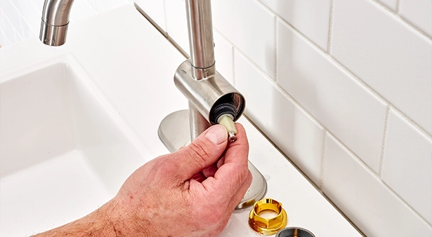 Hand repairing a bathroom faucet beside white tiled wall.