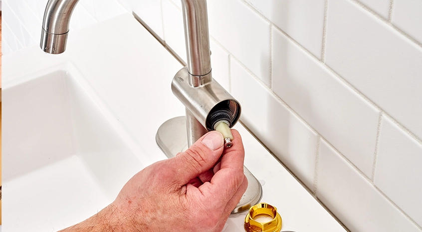 Hand repairing a silver faucet on a white ceramic sink.