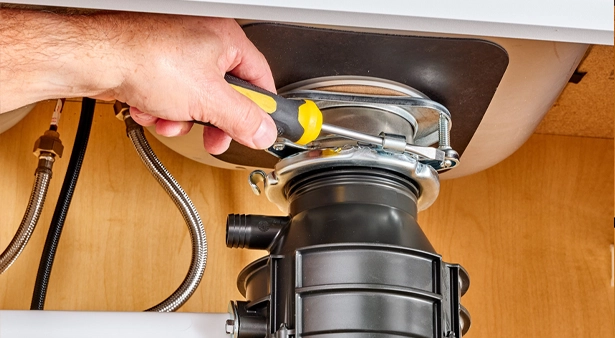 Hand using screwdriver on garbage disposal installation under sink.