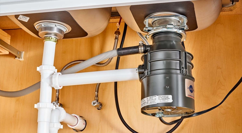 Garbage disposal unit installed under a kitchen sink with visible plumbing pipes.