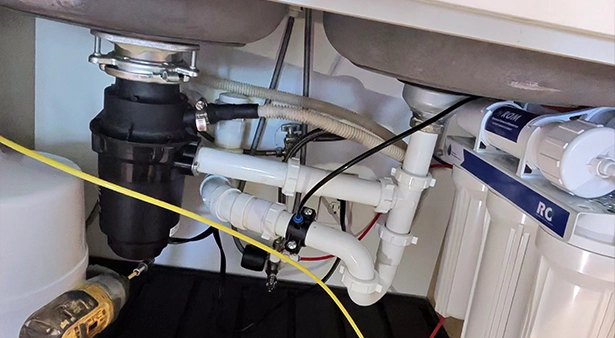 Under-sink plumbing setup with pipes, filters, and a black disposal unit.