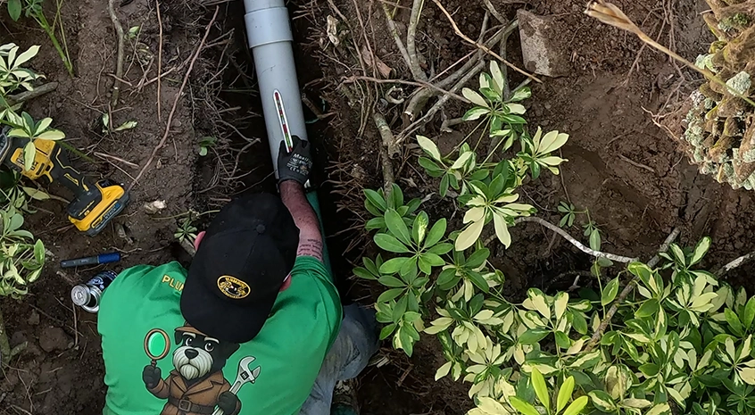 Person in green shirt repairing an underground pipe in a garden.