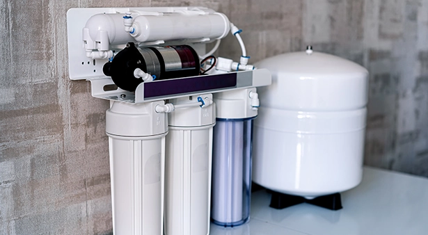 Water filtration system with multiple filters and tank against a textured wall.