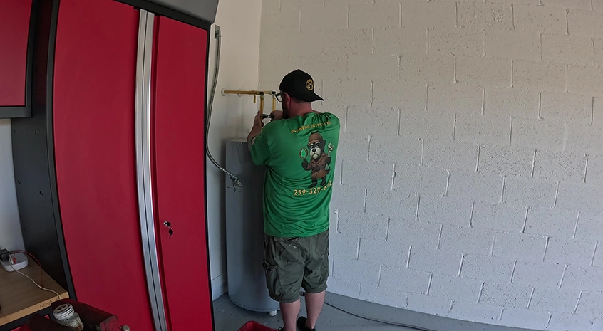 Man installing water heater in a garage with red cabinets.
