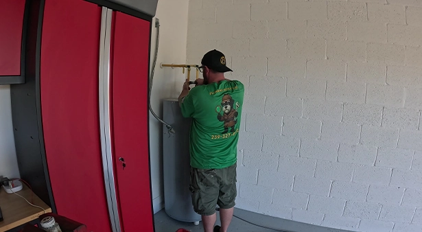 A person in a green shirt fixing plumbing pipes on a wall.