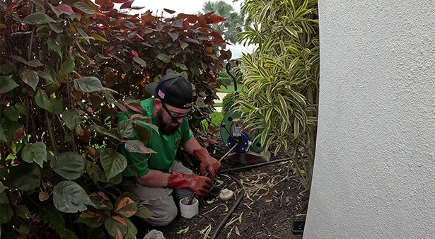 Plumbing technician repairing outdoor hose bib on stucco exterior home wall