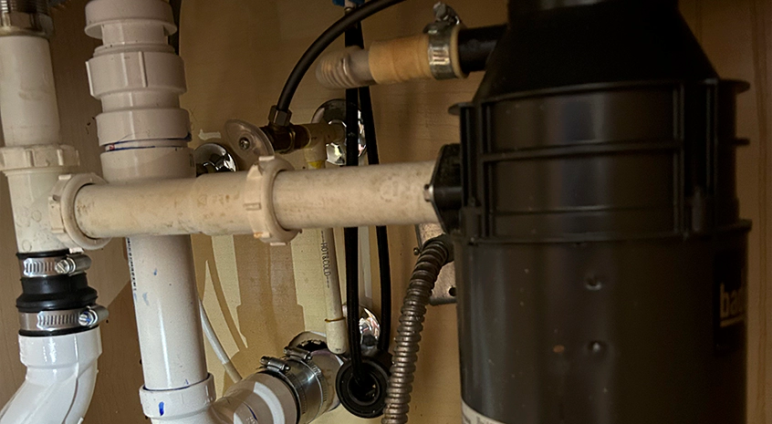 Plumbing under a kitchen sink with pipes and a garbage disposal unit.