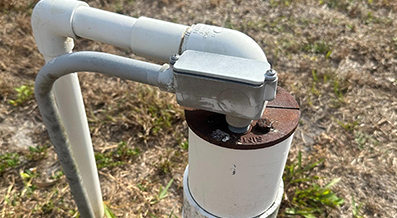 Outdoor plumbing pipe with rusted metal cap on grassy ground.