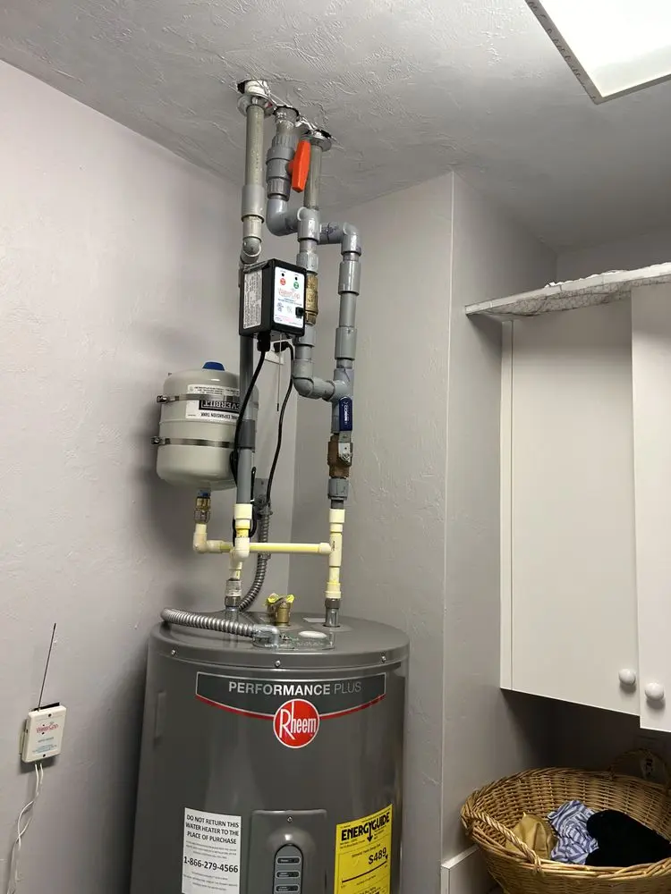Water heater with pipes and pressure tank in a utility room.