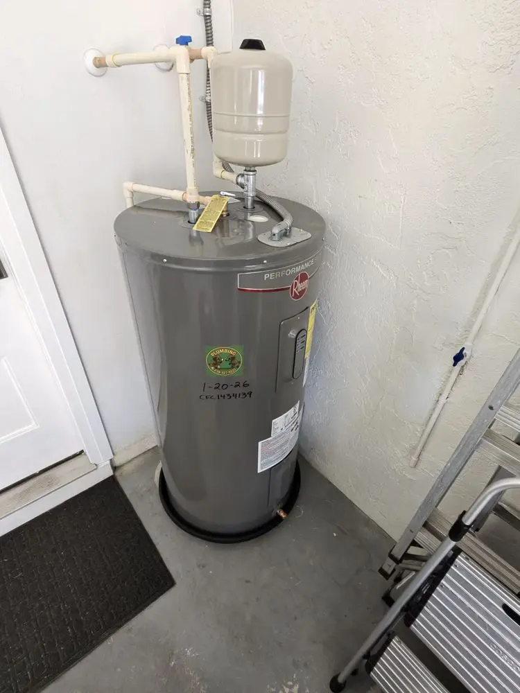 Gray water heater tank in a utility room corner with pipes attached.