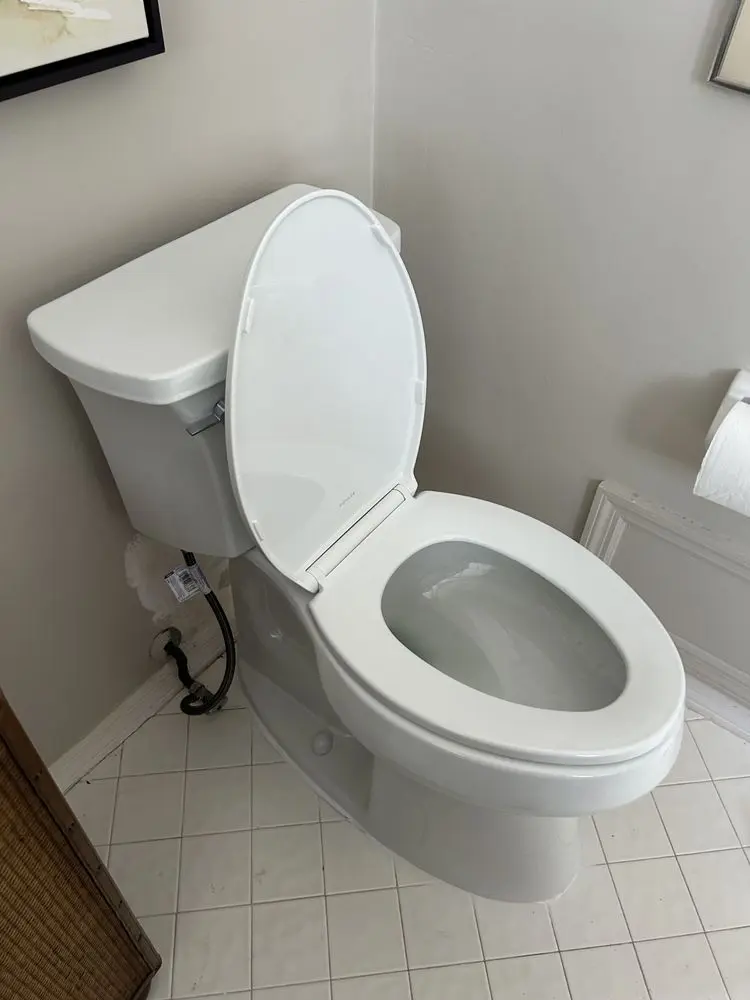 White toilet with open lid on tiled bathroom floor.