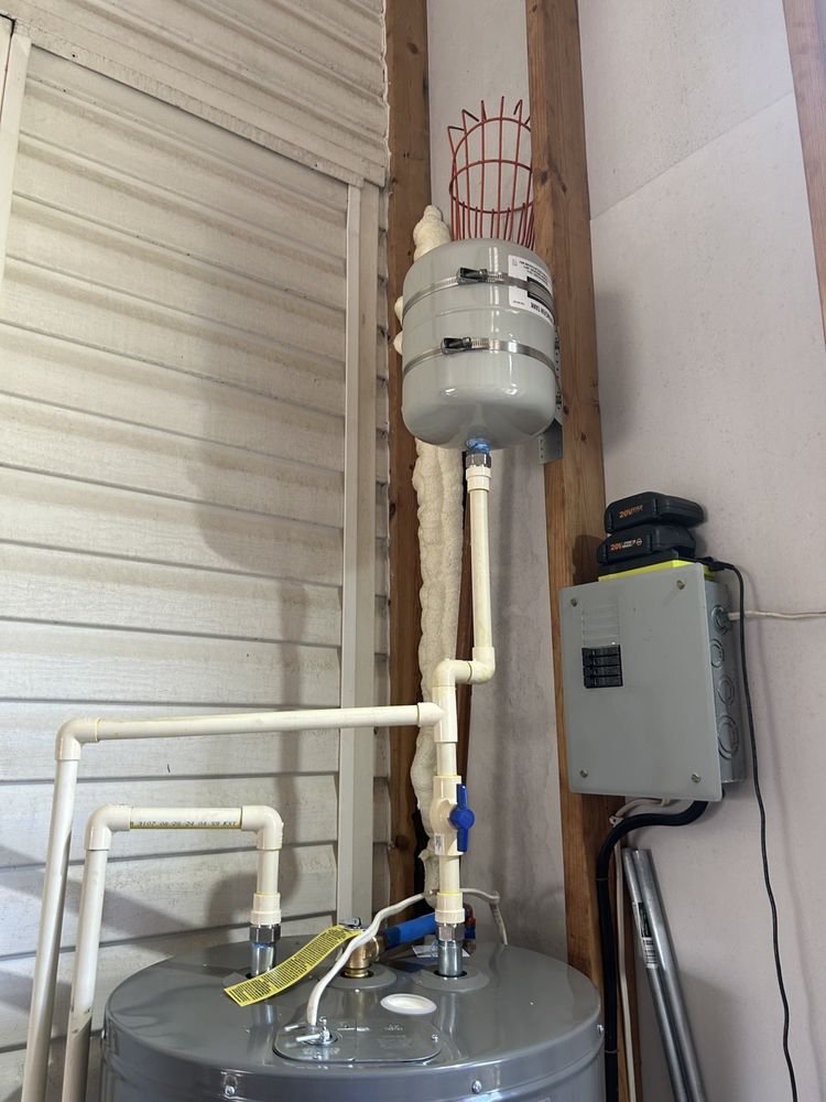 Water heater with pipes and pressure tank in a utility room.