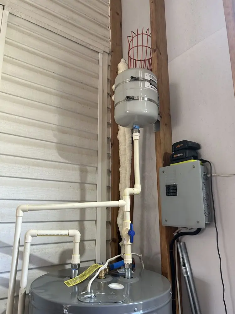 Water heater with pipes and pressure tank in a utility room.