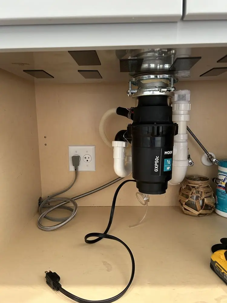 Under-sink garbage disposal unit with visible plumbing and electrical outlet.