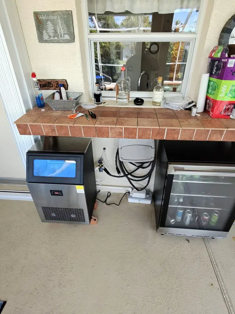 Tile countertop with appliances, bottles, and a small fridge below.