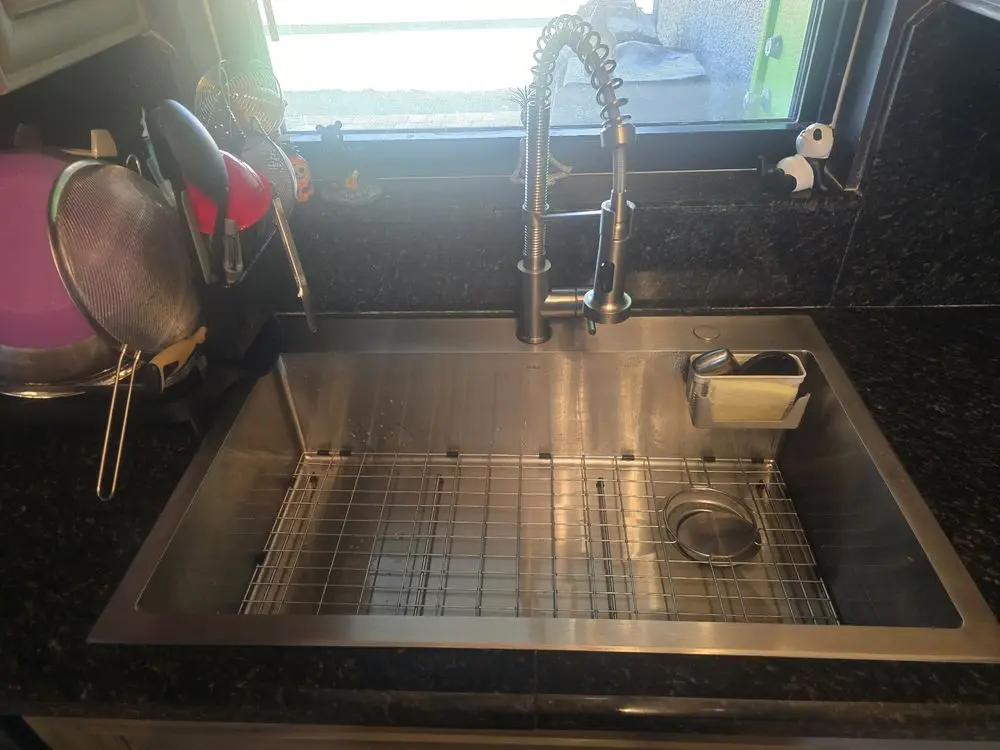 Stainless steel kitchen sink with a coiled faucet and drying rack.