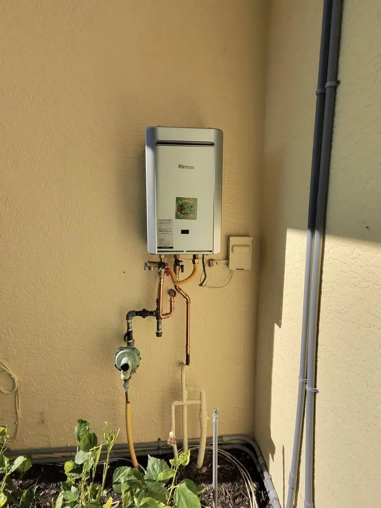 Wall-mounted water heater with pipes on a cream-colored exterior wall.