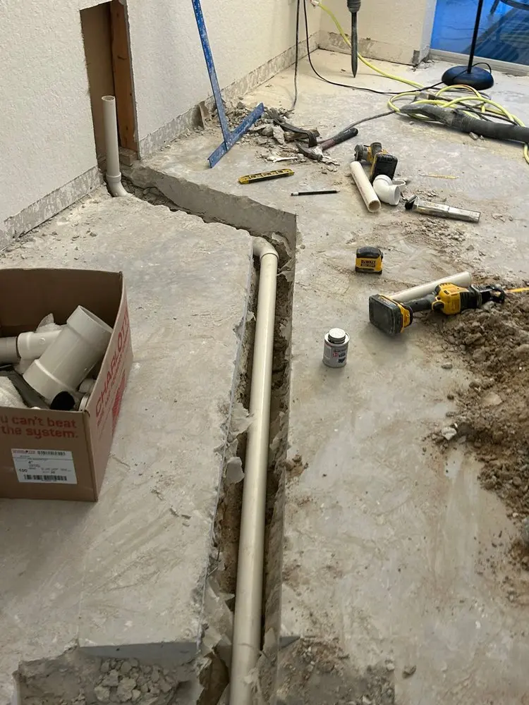 Floor renovation with exposed drainage pipes and scattered plumbing tools.