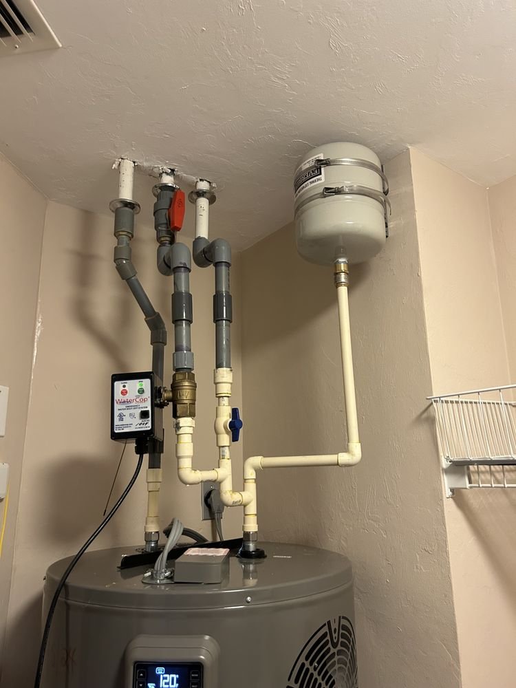 Water heater with connected pipes and a small expansion tank on the wall.