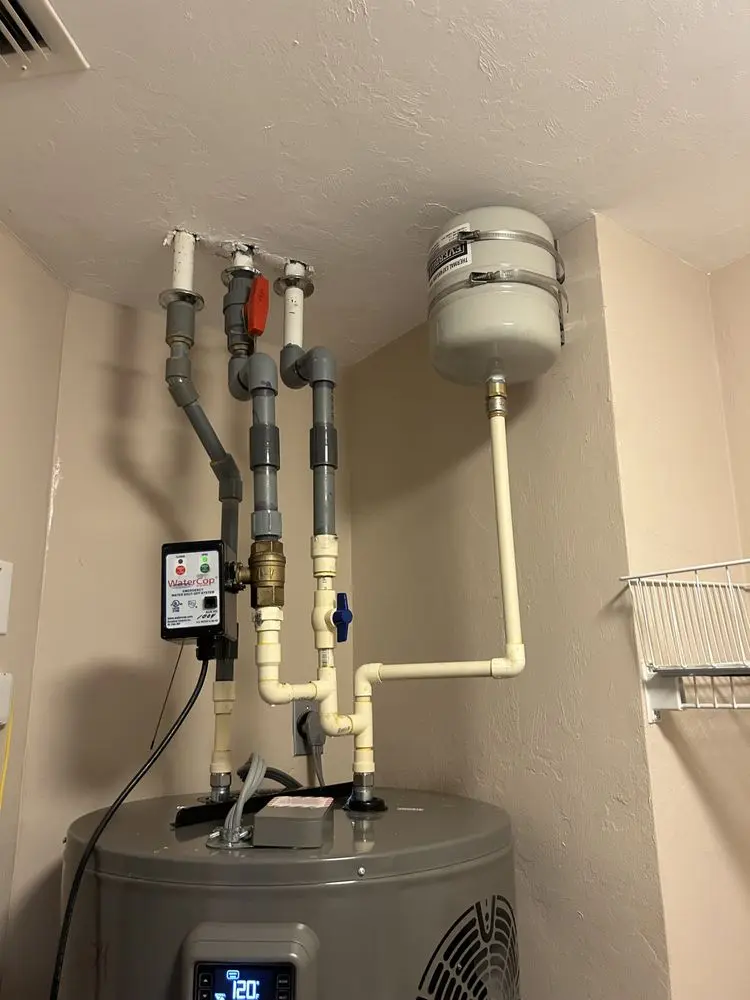Water heater with connected pipes and a small expansion tank on the wall.