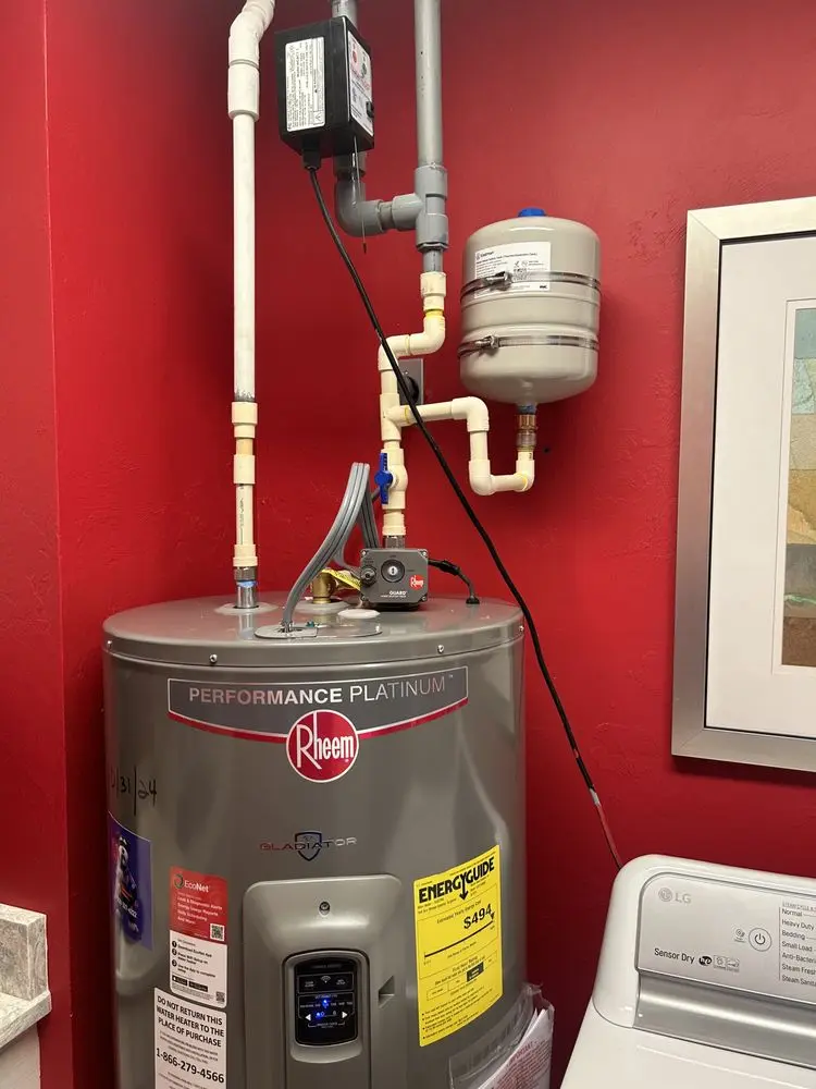 Water heater with pipes and pressure tank in a red-walled room.