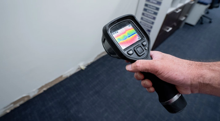 A hand holding a thermal imaging camera inspecting a wall for leaks.