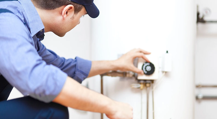 Man in cap adjusting a water heater control knob.