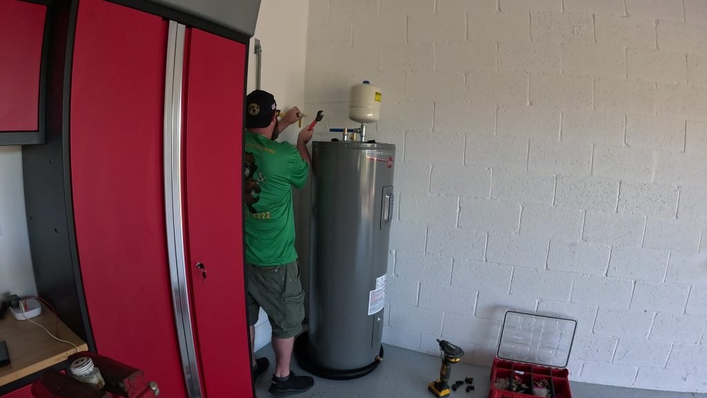 Man repairing water heater next to red cabinet in garage.