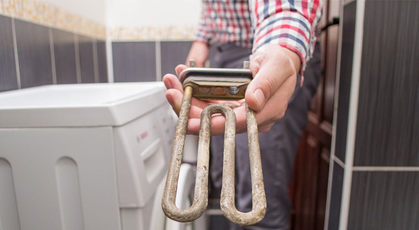 Person holding a corroded water heater element in a bathroom.