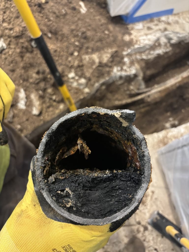 Rusty, corroded cast iron pipe clogged with debris, held by a gloved hand.